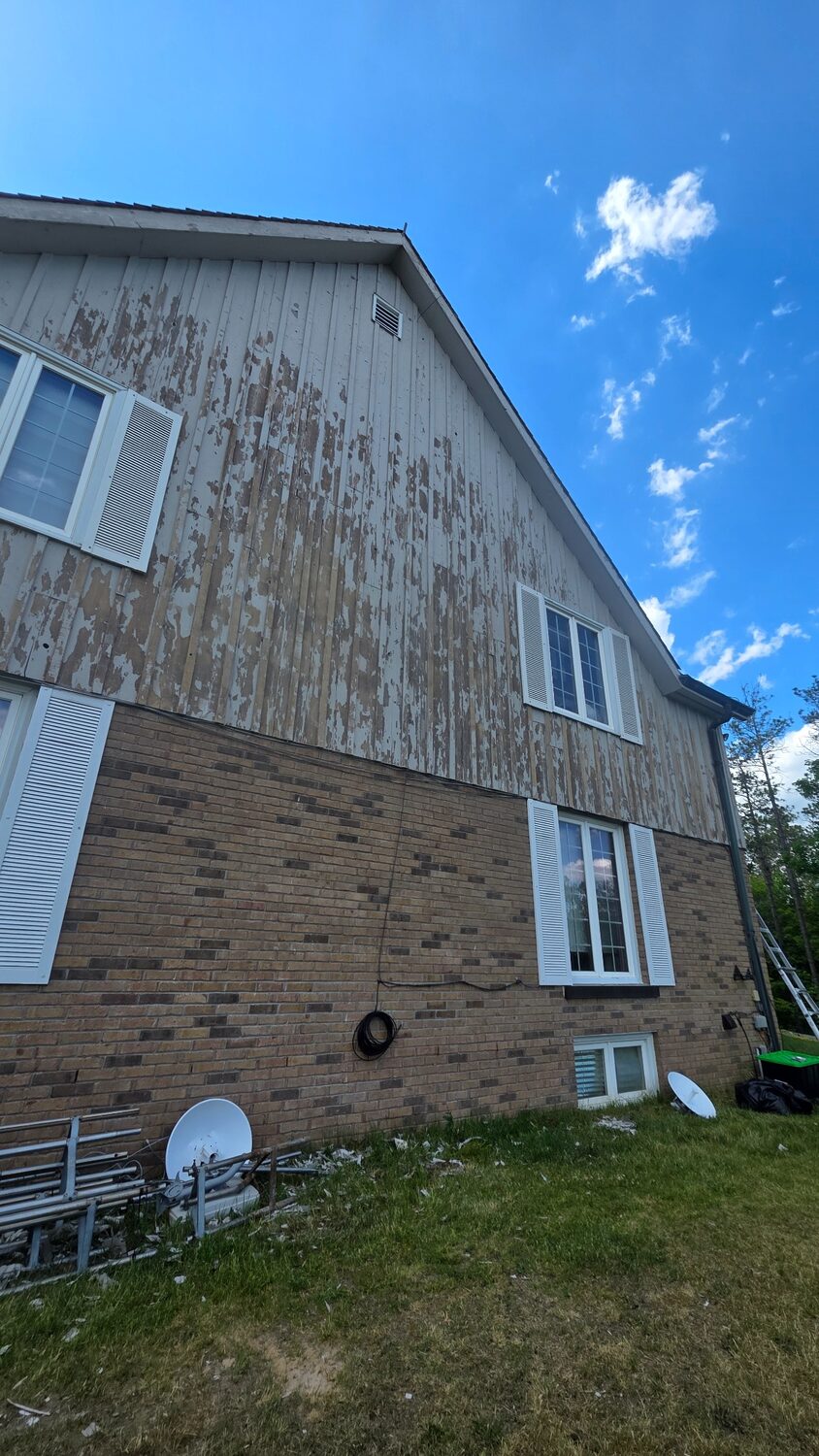 House wall after tower removal with tower sections and dish hardware stacked on site.